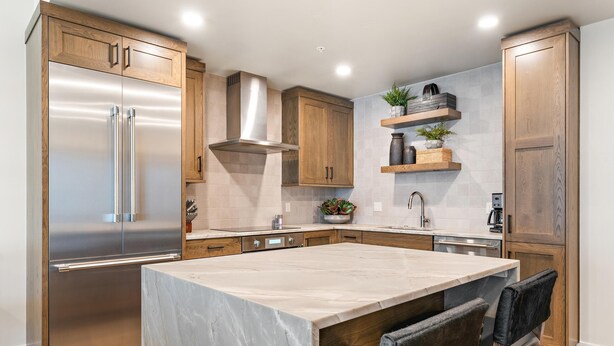 Una cocina moderna con armarios de madera, electrodomésticos de acero inoxidable, una isla de mármol y una estufa integrada.