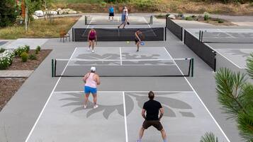 An outdoor tennis court with multiple players, benches, and a surrounding landscaped area.