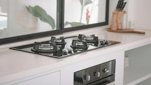 A kitchen with a gas stove, a window with a plant, and a knife block. - Arrova Bali Berawa, Canggu by Sandara (Jimbaran)