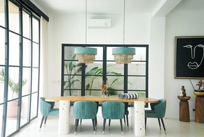 A dining area with a wooden table, teal chairs, and a large window with black frames.