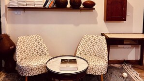A room with two patterned chairs, a small round table with a book, and three framed photographs on the wall. - The Ocean Breeze bungalow (Sidi Kaouki)