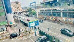Une vue de rue avec un panneau indiquant un espace de stationnement, un bâtiment recouvert de graffitis et une grande structure cylindrique sur laquelle on peut lire le mot « SCI ».