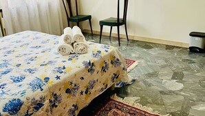 Une chambre d’hôtel avec un lit, deux chaises, une poubelle et un tapis à motifs.