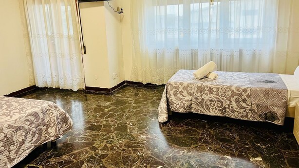 Une chambre d’hôtel avec deux lits, un téléviseur à écran plat fixé au mur et une fenêtre avec des rideaux légers.