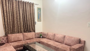 A living room with a sectional sofa, a glass coffee table, and a potted plant.