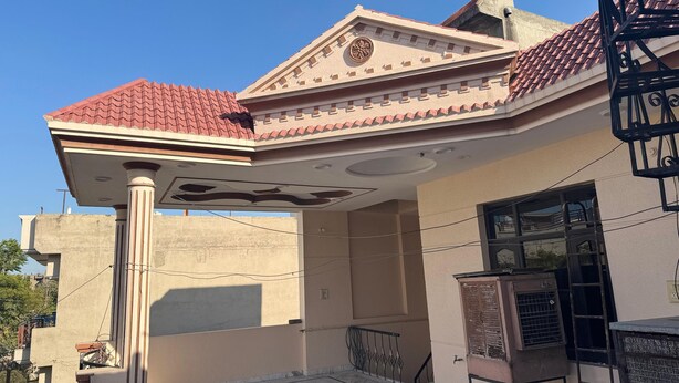 A residential building with a red-tiled roof, a balcony with a metal railing, and a decorative ceiling design.