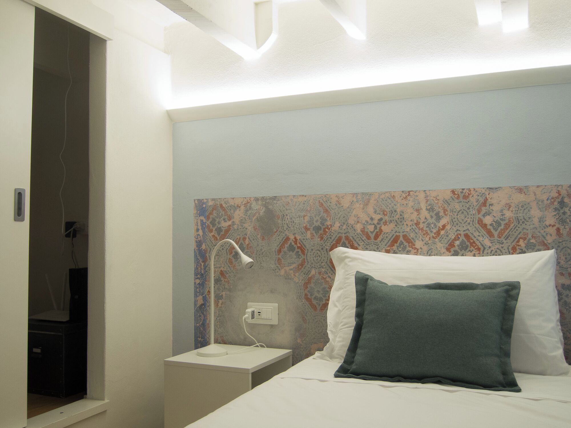 A hotel room with a bed, a nightstand, a wall-mounted lamp, and a patterned wallpaper.