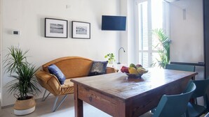 A dining area with a wooden table, blue chairs, a sofa with cushions, framed pictures on the wall, and a television. - Bright 3 Bed Rooms Orti Oricellari (Florence)