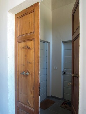 Eine Holztür mit einem Metallgriff, eine weiße Wand und ein Fliesenboden.