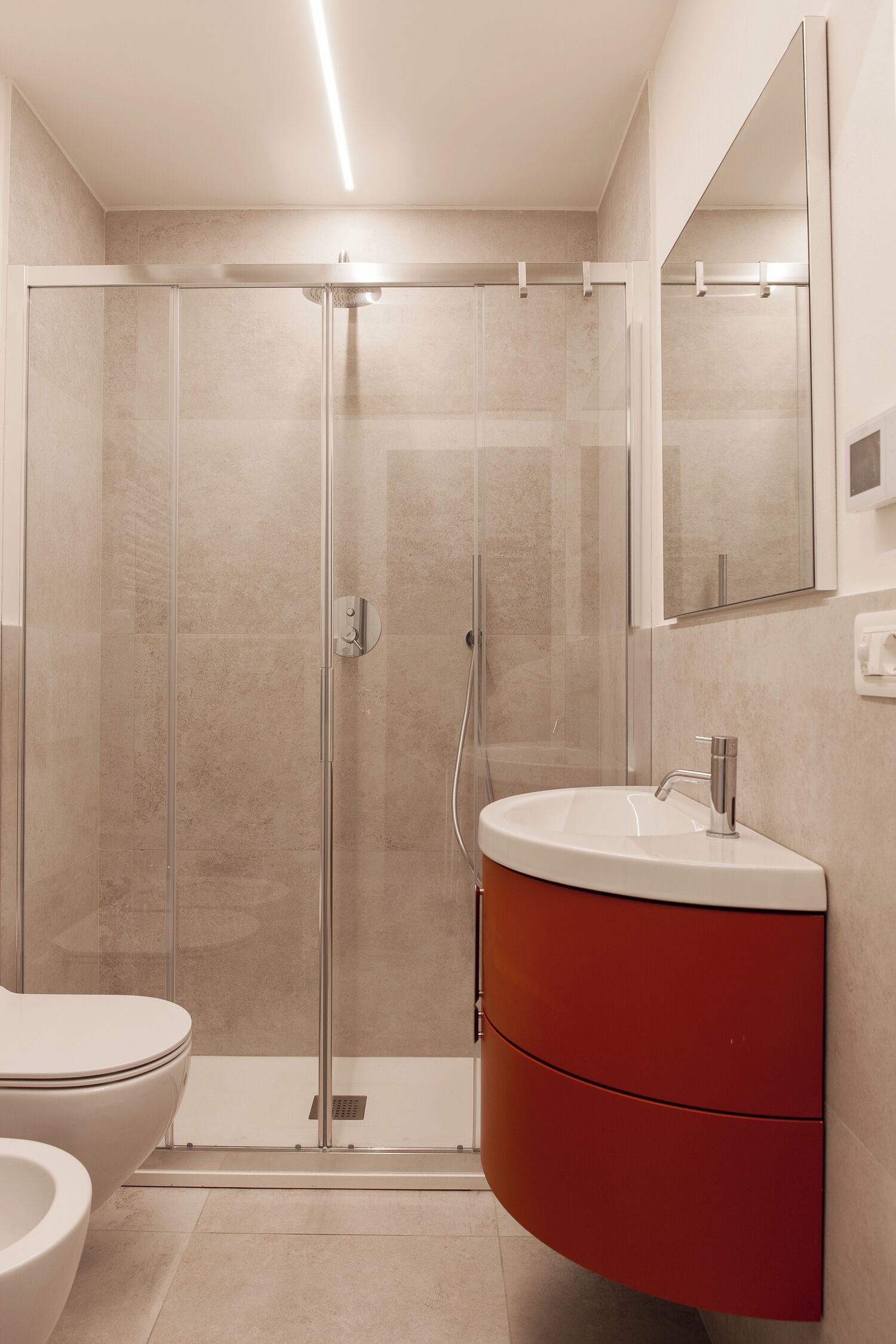 A modern bathroom with a glass-enclosed shower, a white sink, and a red vanity.