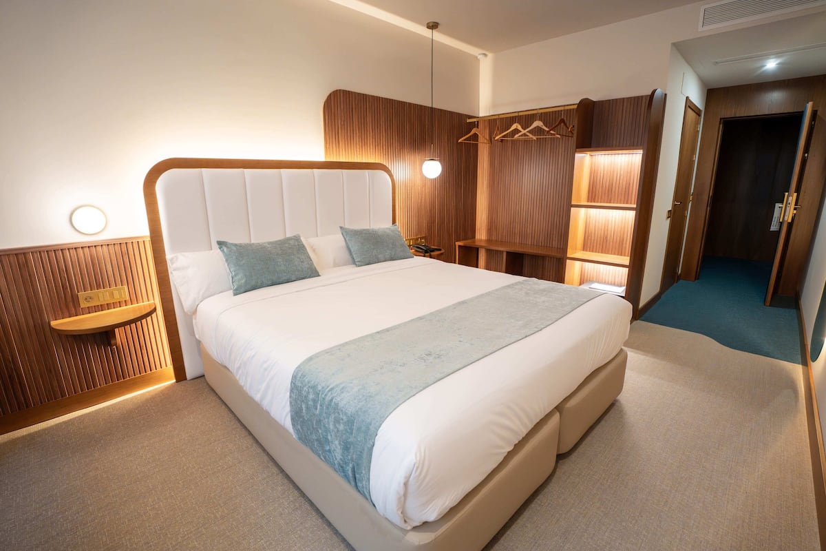 Ein modernes Hotelzimmer mit einem großen Bett, Holzvertäfelung, einem Nachttisch und einer Pendelleuchte.