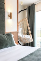 Una cama con una silla colgante, una lámpara de pared y una ventana con cortinas.