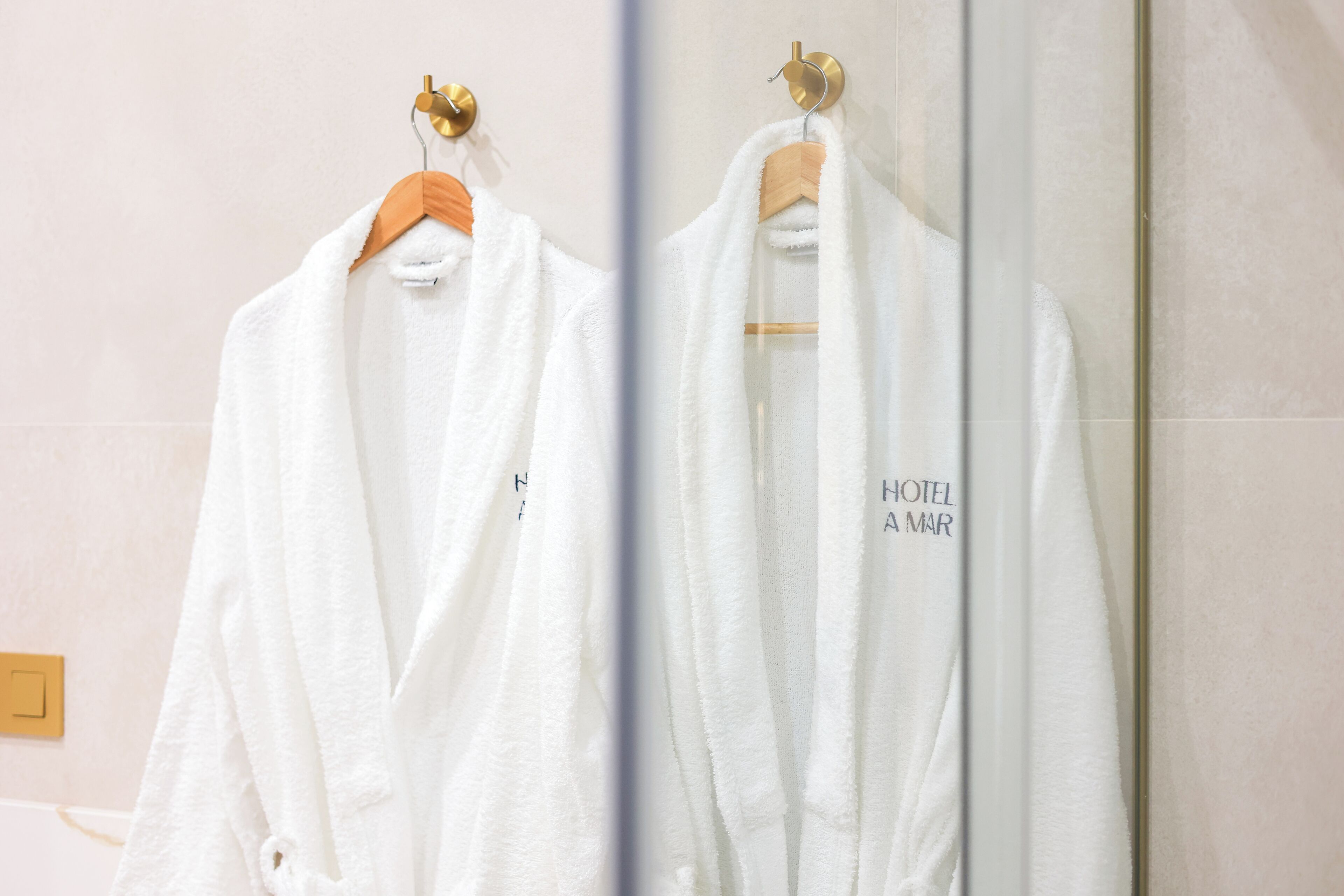 Una bata blanca colgada de una percha de madera en un baño, con un espejo que refleja la bata.