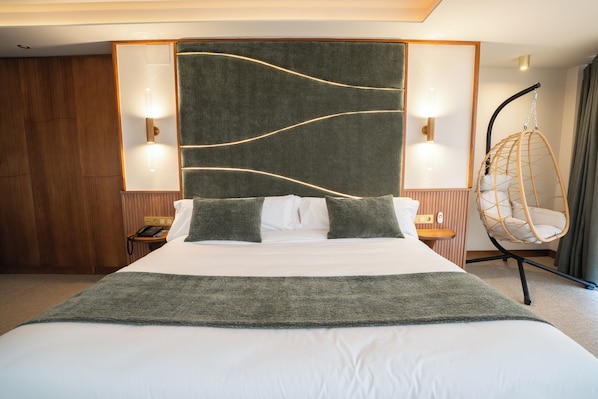 Una cama bien hecha con un plaid gris, un sillón colgante y dos lámparas de noche.