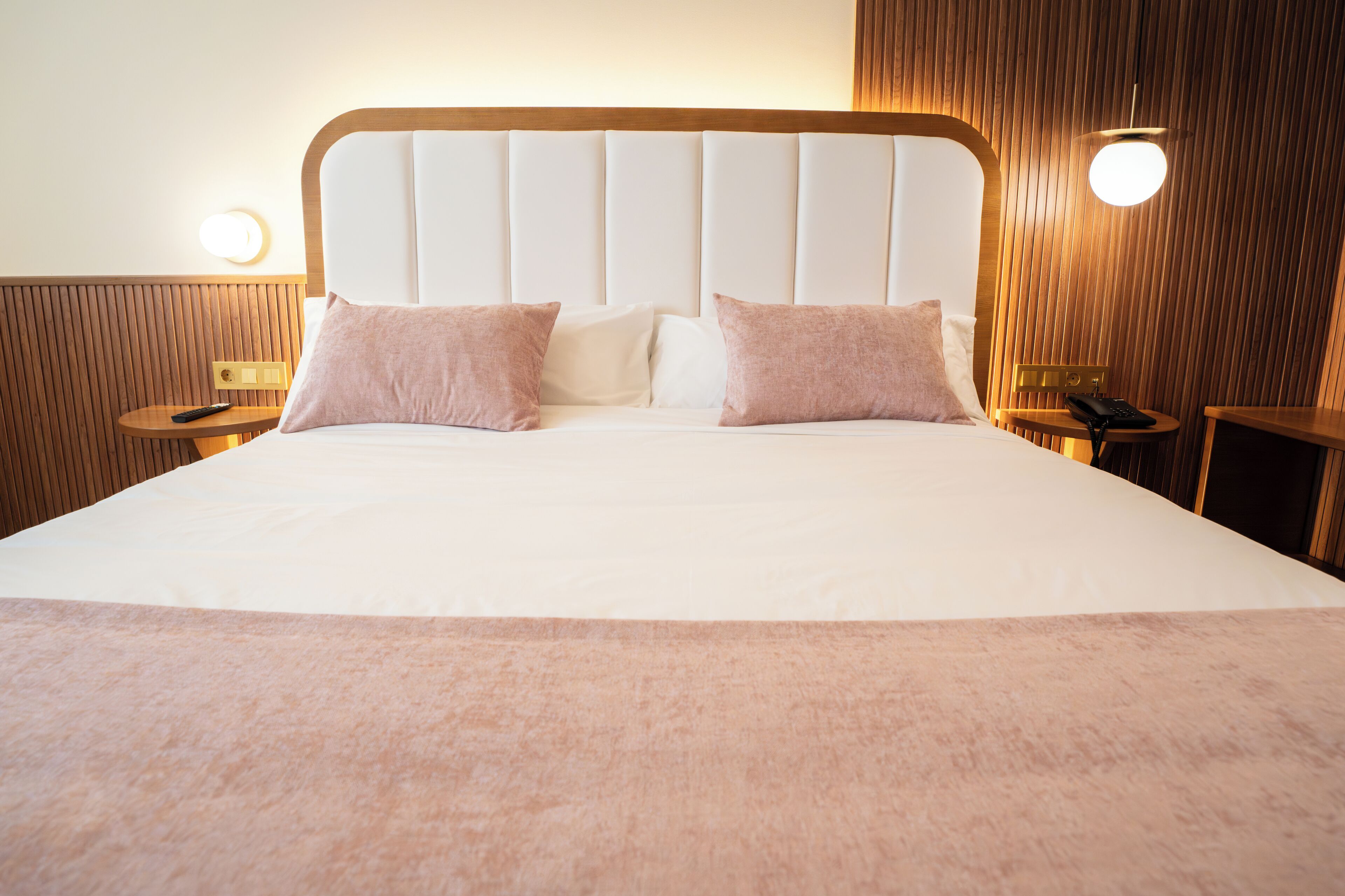 A neatly made bed with a wooden headboard, two bedside tables with lamps, and a wall-mounted light fixture.