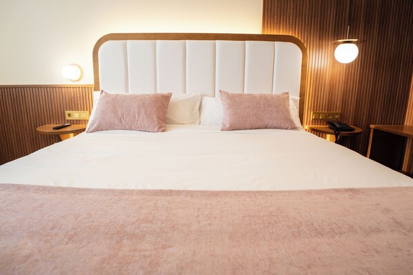 A neatly made bed with a wooden headboard, two bedside tables with lamps, and a wall-mounted light fixture. - Hospedium Hotel A Mar (Villafranca de los Barros)