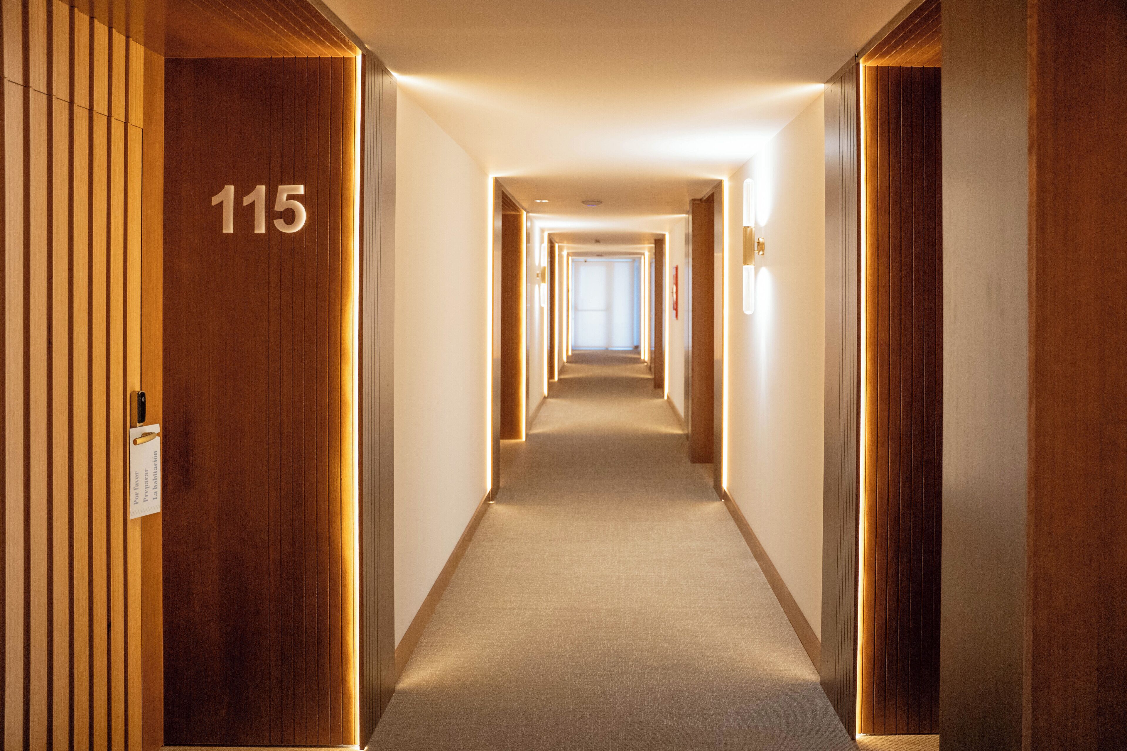 Un pasillo de hotel con paneles de madera, suelo alfombrado y un cartel con el número 115 en la pared.