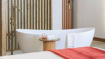 Un baño moderno con una bañera independiente, un revestimiento de madera y una mesita redonda con una toalla.