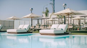 Un área de piscina con sillones reclinables y sombrillas.