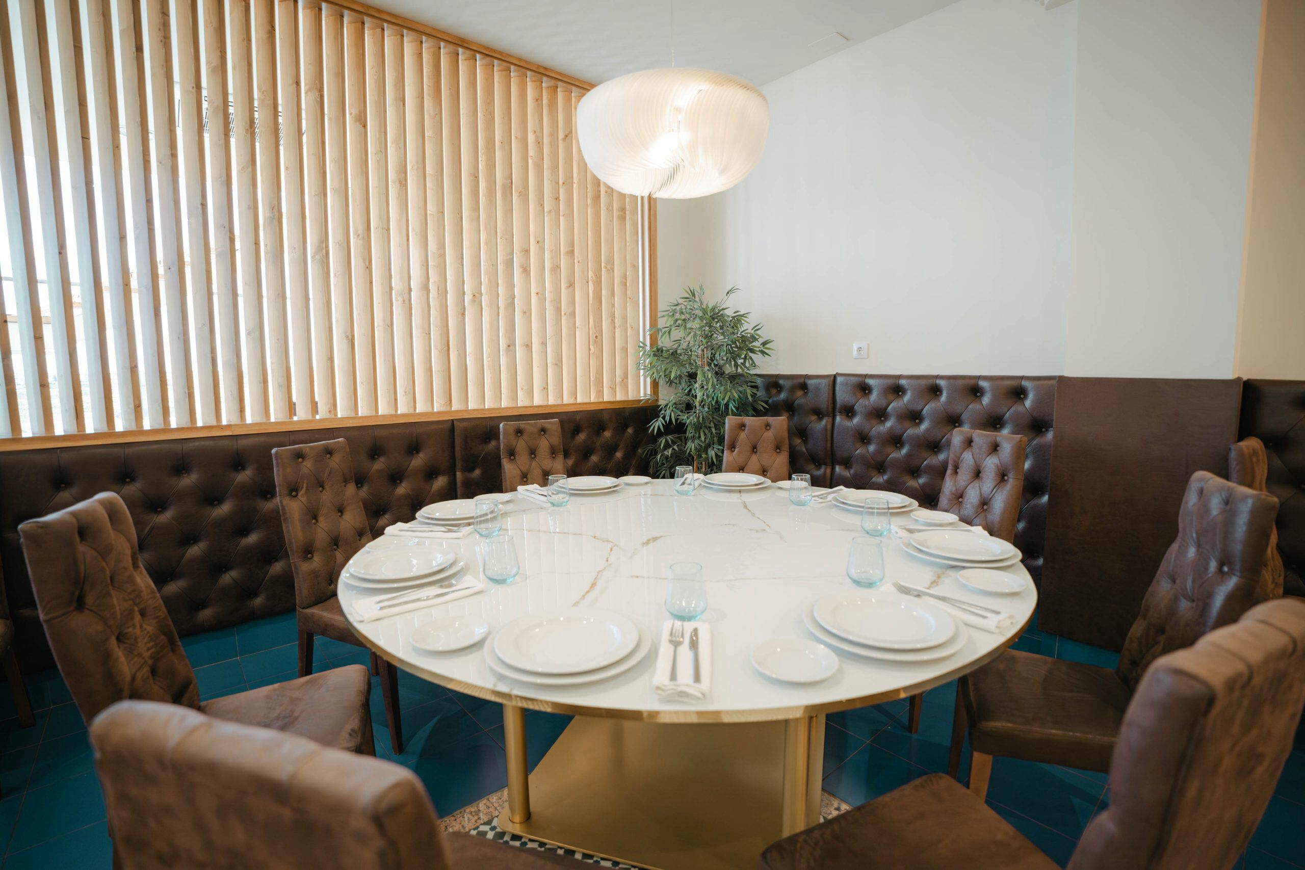 Een ronde tafel met witte borden en glazen, omringd door bruine stoelen met bekleding.