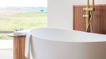 Un baño moderno con una bañera independiente, un taburete de madera y vistas a un paisaje verde.