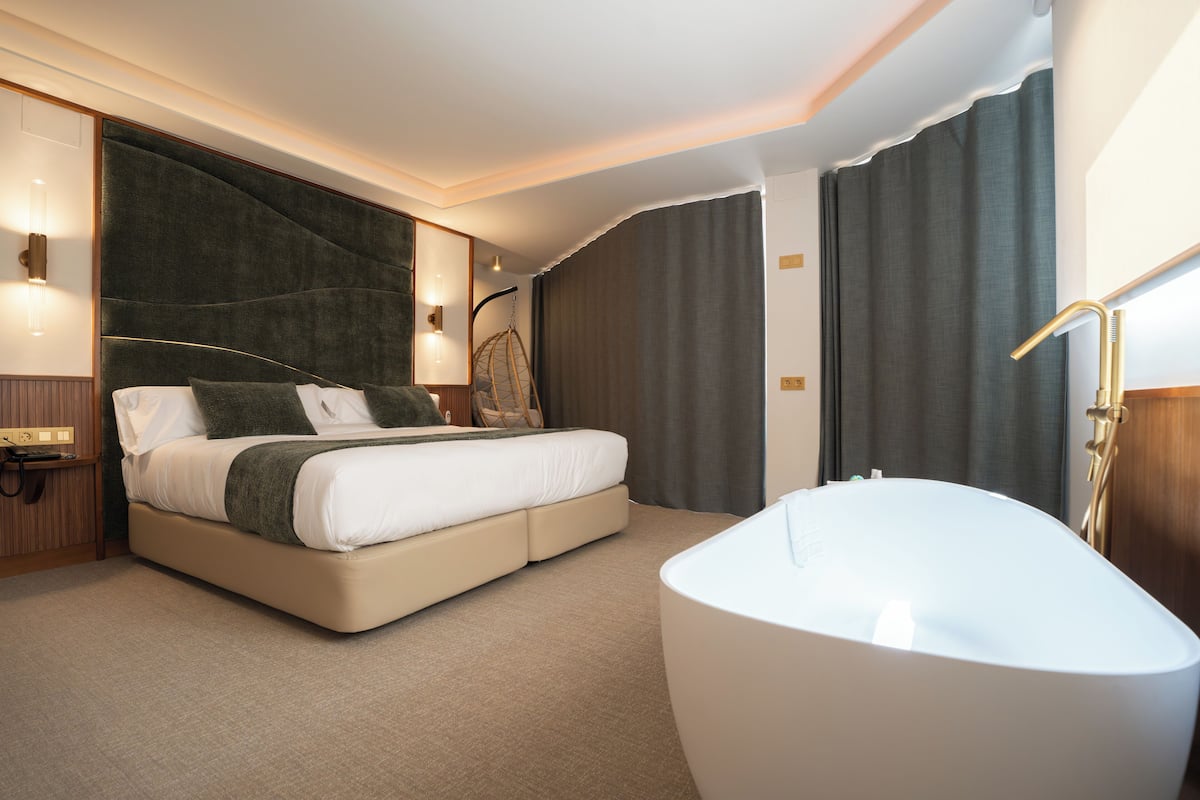 Ein modernes Hotelzimmer mit einem großen Bett, einer separaten Sitzecke, einer Badewanne und einem Hängekorbsessel.