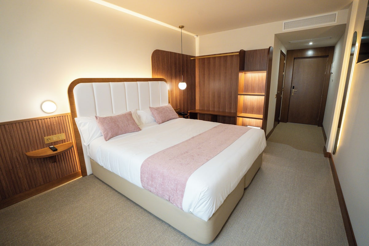 Ein modernes Hotelzimmer mit einem großen Bett, Nachttischen, einem eingebauten Kleiderschrank und einem kleinen Schreibtisch.