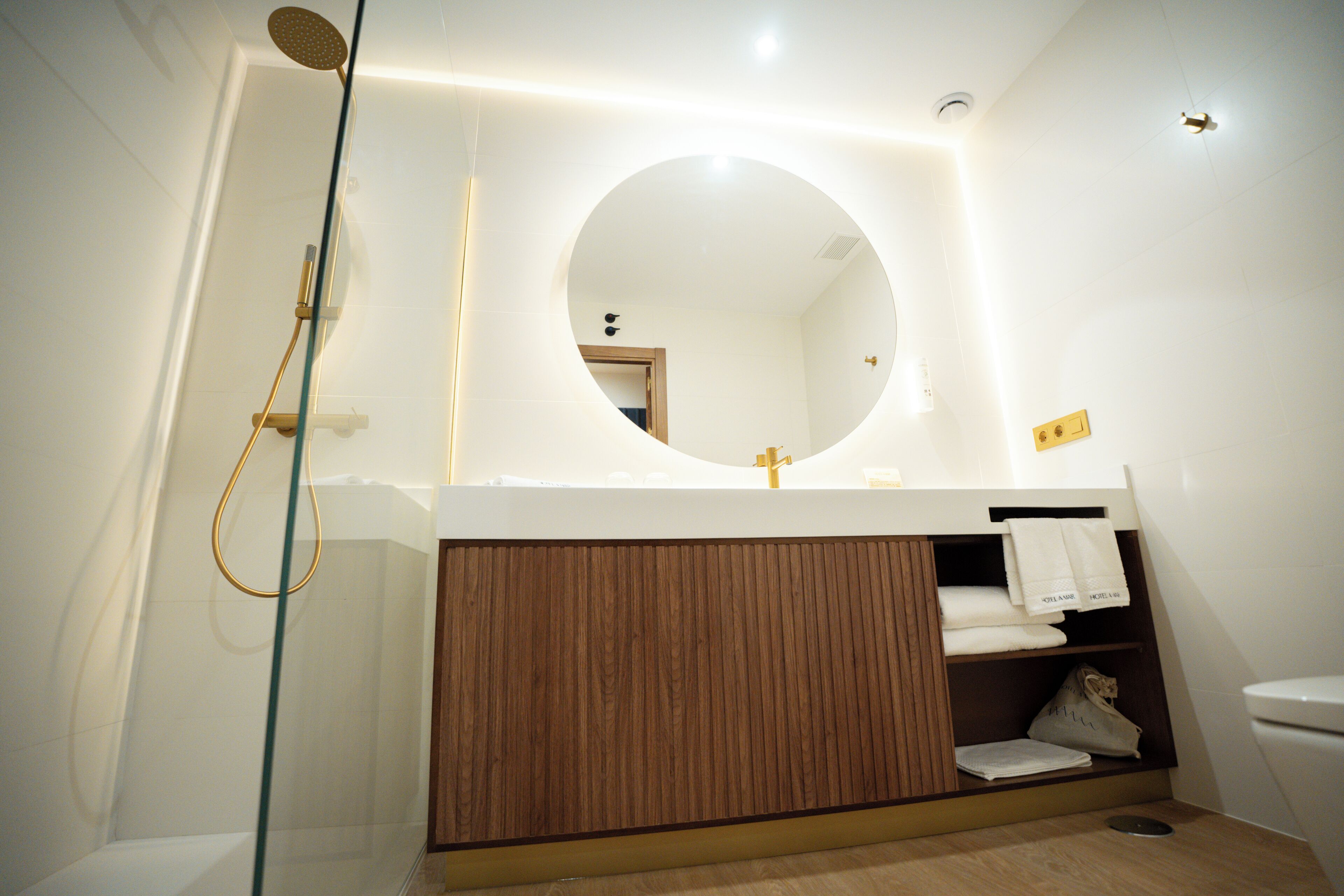A modern bathroom with a glass-enclosed shower, a wooden vanity, and a round mirror above the sink.