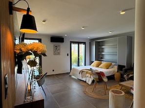 Een moderne slaapkamer met een bed, een stoel, een bureau en een groot raam.