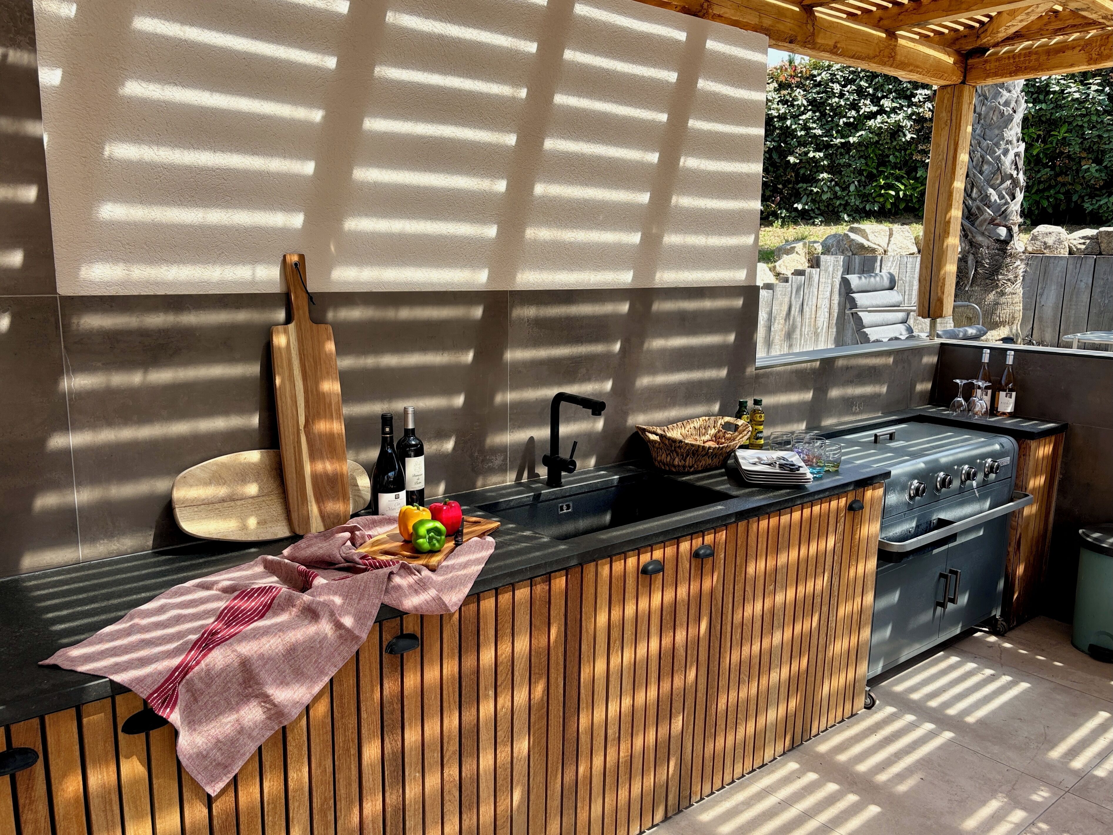 Una cocina al aire libre con mostrador de madera, un lavamanos y una parrilla.
