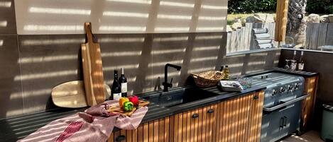 Una cocina al aire libre con mostrador de madera, un lavamanos y una parrilla.