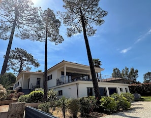 Een gebouw met twee verdiepingen en een balkon, omgeven door bomen en struiken.