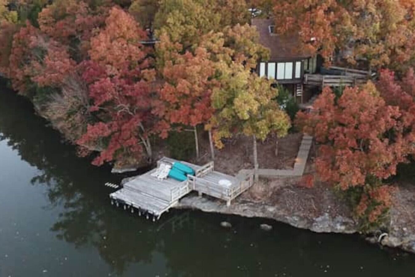 Vista aérea de una propiedad junto al lago con un muelle, un edificio pequeño y una terraza de madera.