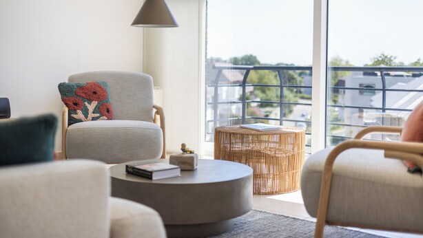 A modern living room with a grey armchair, a round coffee table, and a wicker ottoman. - 3 bedroom accommodation in Sint-Idesbald (Sint-Idesbald)
