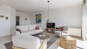 A modern living room with a sofa, coffee table, and chairs. There is a flat-screen TV and a radiator. - 3 bedroom accommodation in Sint-Idesbald (Sint-Idesbald)