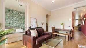 A modern living room with a leather sofa, glass coffee table, and a dining area with a wooden table and chairs. - Enjoy Apartments Donna (Barcelona)