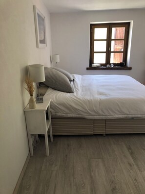 Une chambre à coucher avec un lit, une table de chevet, une lampe, une fenêtre et un tableau au mur.