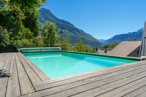 A swimming pool with a wooden deck, surrounded by greenery and mountains in the background. - Contemporary Design & Architecture: Duplex, Puy Saint Vincent/Pelvoux, Vallouise (Les Vigneaux)