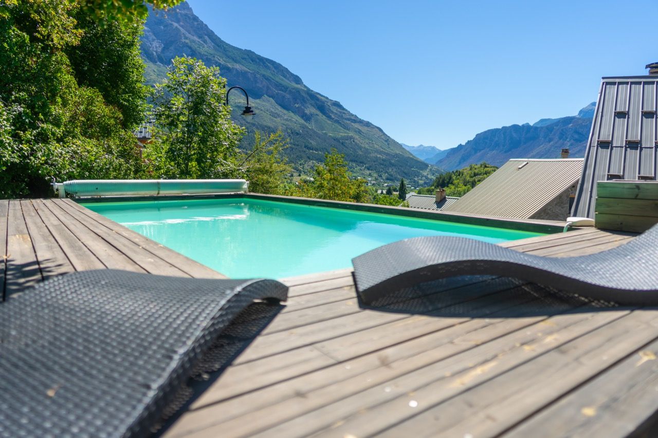 A wooden deck with a pool, lounge chairs, and a mountain view.