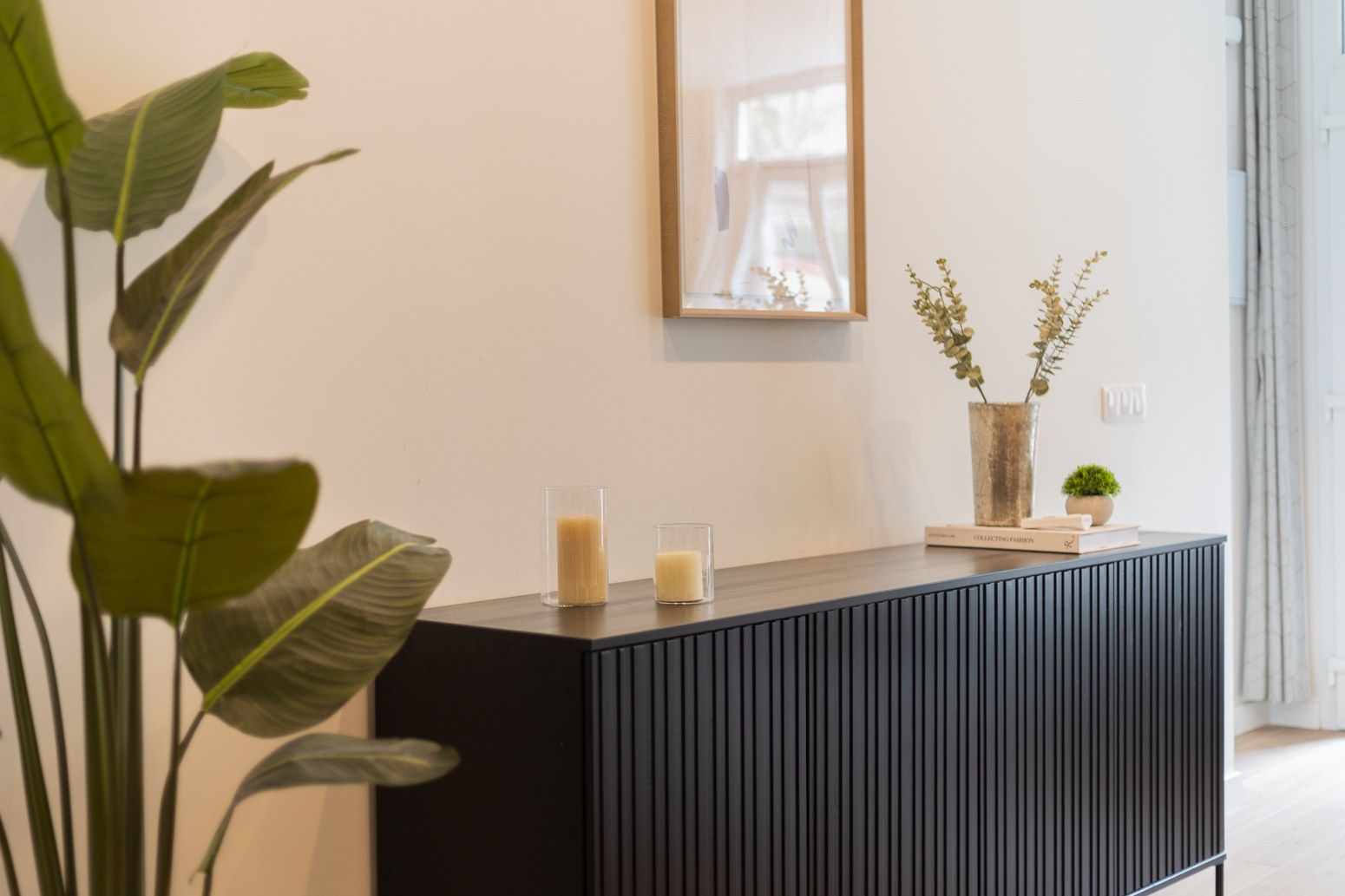 Un interior moderno con una consola de mesa oscura, un espejo enmarcado y plantas decorativas.