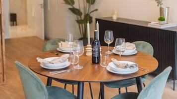 Una mesa de comedor dispuesta con platos, cubiertos, copas y una botella de vino, rodeada de sillas.