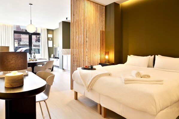 Een hotelkamer met een bed, een bureau met een lamp, een stoel, een eettafel met borden en uitzicht op buiten.