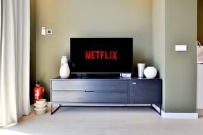 Een moderne woonkamer met een flatscreen televisie op een donker houten dressoir, een vaas en een brandblusser.