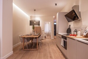 A modern kitchen with a dining area, wooden flooring, and a pendant light.