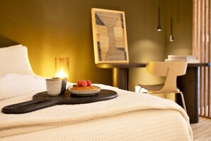 A neatly made bed with a tray of food, a cup, and a plate with fruit.