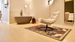 A modern bathroom with a freestanding bathtub, a chair, and a patterned rug.