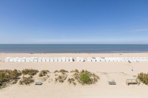 Ein Strand mit Reihen weißer Strandhütten und einem sandigen Vordergrund mit etwas Vegetation.