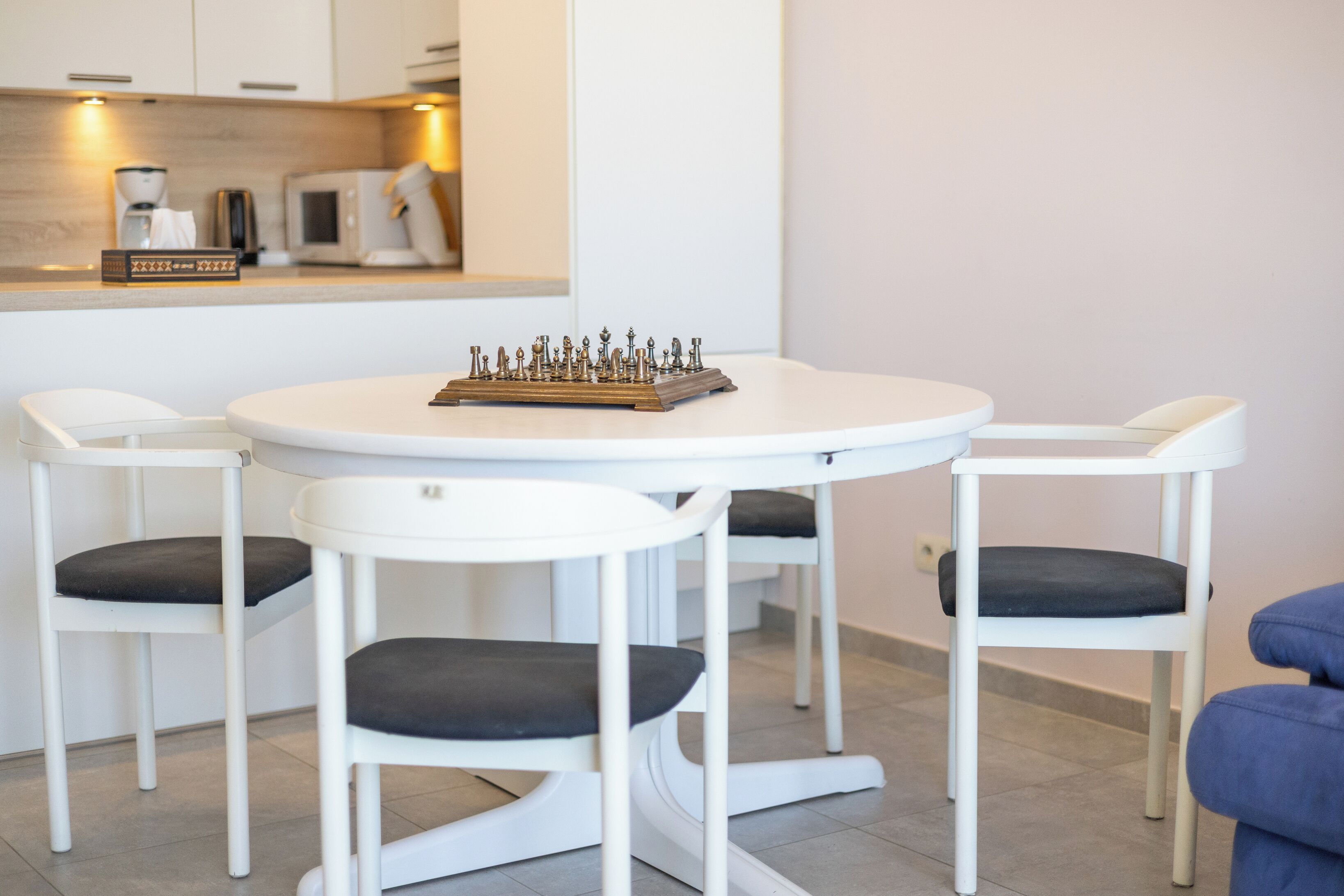 Un espace repas moderne avec une table ronde et quatre chaises blanches dotées de coussins foncés.