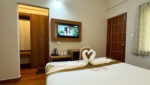 Een hotelkamer met een bed, een aan de muur bevestigde televisie, een houten kledingkast en een bureau met een waterkoker.