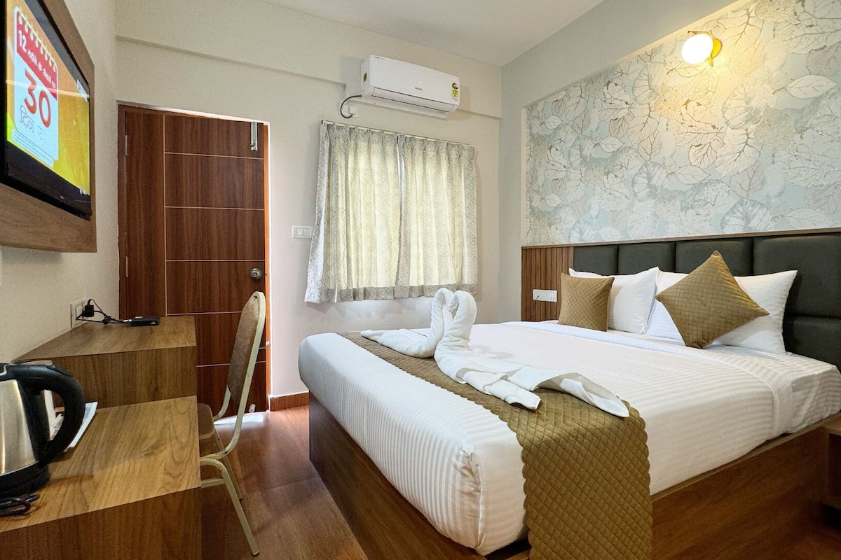 A hotel room with a bed, a desk with a kettle, a wardrobe, and a wall-mounted air conditioner.